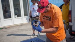 Gépátvétel Gábor verseny végén a megbontott motorok alkatrészeit vizsgálja. A kezében egy Piaggio henger látható, az ötszögletű kialakításról messziről felismerni (a hengert, nem Gábort)