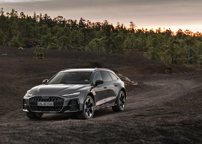 Audi A6 allroad (pearlgrey) in a three-quarter front view on unpaved ground at dusk.