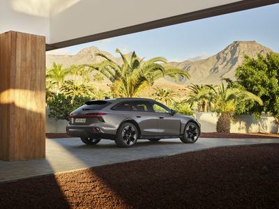 Static three-quarter rear view of the Audi A6 allroad (pearl gray) set in modern architecture with a striking mountain panorama in the background (static shot)