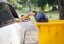 A female hand  holding garbage bag into trash out of a car. Environmental pollution.