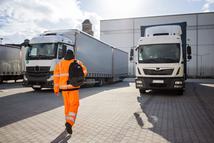 Rear view of man in reflective clothing walking with bag arriving to work. Commercial dock worker arriving to job.