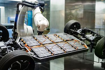 An industrial robotic arm installs a battery pack on an electric car chassis, showcasing advanced technology in automotive manufacturing and sustainable transportation solutions.