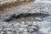 Close-up of potholes on a wet urban road with a passing vehicle, illustrating damaged infrastructure, poor road conditions, traffic safety risks, and the need for road maintenance in city environments.