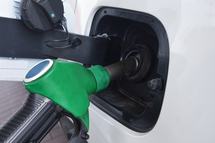A green fuel nozzle inserted into the fuel tank of a white modern car