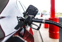 black luxury car refueling in the gas station and blurry red gasoline barrels in the background