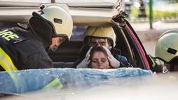 Close up shot through cut windshield of two  firefighters helping injured female driver in shock, one is holding her head.