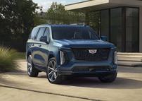 Front ¾ view of the 2025 Cadillac Escalade Sport Platinum in Deep Sea Metallic with a house and greenery in the background.